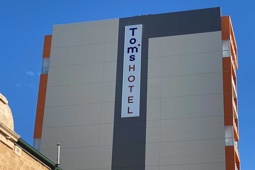 Un bâtiment de l'hôtel gris de plusieurs étages avec Tom's Hotel écrit verticalement sur un signe