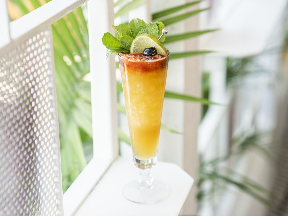 Wild's Mango Rye Tie dans un grand verre avec de la menthe, une cerise et du citron vert comme garniture.