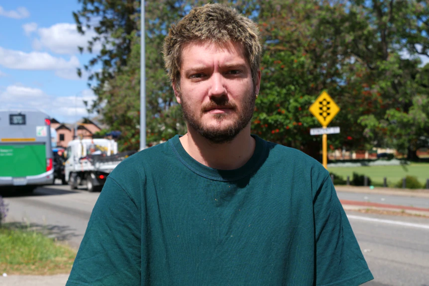 Un homme en chemise verte se tient devant une route principale